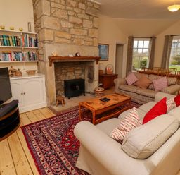 A living room with sofas and pillows around a wooden coffee table and a stone fireplace with bookshelves at Armstrong Cottages No2 Bamburgh