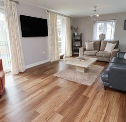 A living room with two sofas a chair a coffee table a wall-mounted TV and windows with curtains at Assisi Apartment in Alnmouth