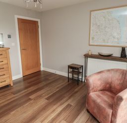 A room with wooden flooring a wooden door a chest of drawers a small table a console table with decorative items a map on the wall and a velvet armchair at Assisi Apartment in Alnmouth
