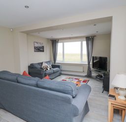 A living room with two gray sofas a television on a stand a window with curtains and a small table with a lamp at Beach View in Seahouses