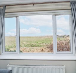 A window with gray curtains framing a view of a grassy field and blue sky at Beach View in Seahouses