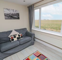 A sitting area with a grey sofa and cushions next to a large window showing a field at Beach View in Seahouses