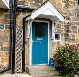 A blue front door with the number 5 on a stone house with plants outside at Begonia House in Alnmouth
