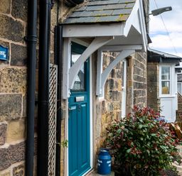 A stone house exterior with a blue door numbered 5 and bushes beside it at Begonia House in Alnmouth