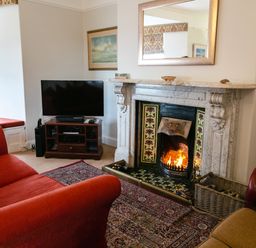 A living room with a fireplace a television on a stand and red sofas at Begonia House in Alnmouth