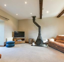 A living room with a brown sofa a wood stove a flat screen tv on a wooden stand and two blue cushions on the floor at Budle Granary in Bamburgh