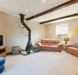 A living room with two brown sofas a black wood stove a television on a wooden stand and ceiling beams at Budle Granary in Bamburgh