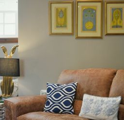 A living room with a brown leather sofa with patterned cushions and three framed artworks above at Budle Granary in Bamburgh