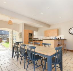 A kitchen with a wooden dining table and blue chairs and an open door showing a garden at Budle Granary Bamburgh