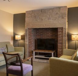 A living room with two sofas a chair and a television set in a brick fireplace at Cheshill Cottage in Alnmouth