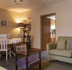 A living room with a green sofa a purple chair a dining table with white chairs and a floor lamp at Cheshill Cottage in Alnmouth