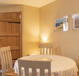 A dining area with a round table covered with a tablecloth and four chairs near a wooden door at Cheshill Cottage in Alnmouth
