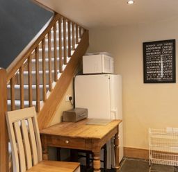 A wooden staircase next to a wooden table with a chair and a refrigerator with a microwave on top at Cheshill Cottage in Alnmouth