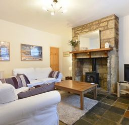A living room with white sofas wooden coffee table stone fireplace and television at Crier Cottage Alnwick