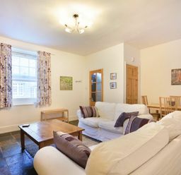 A living room with white sofas purple cushions wooden coffee table dining table and chairs at Crier Cottage in Alnwick