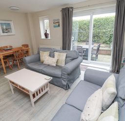 A living room with two blue sofas a white coffee table wooden dining table and chairs sliding glass doors to a patio at Curlew Cottage in Seahouses