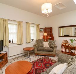A living room with two sofas a television on a wooden stand and a dining table with four chairs at Glebe Cottage in Bamburgh