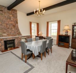 A dining room with a stone fireplace a table with six chairs and a cabinet at Glebe House in Bamburgh