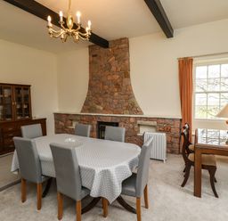 A dining room with a dining table covered by a polka dot tablecloth and six chairs a stone fireplace a wooden cabinet a small table with two chairs and a lamp at Glebe House in Bamburgh