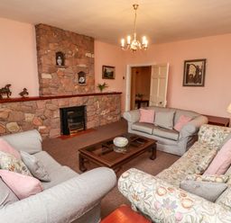 A living room with sofas around a wooden coffee table and a stone fireplace at Glebe House in Bamburgh