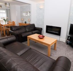 A living room with black leather sofas a wooden coffee table and a dining area at Bay View in Amble