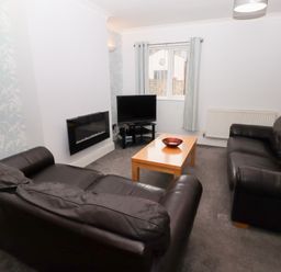 A living room with two black leather sofas a wooden coffee table with a bowl a wall-mounted electric fireplace and a television on a stand at Bay View in Amble