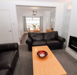 A living room with black leather sofas a wooden coffee table and dining area with table and chairs at Bay View in Amble