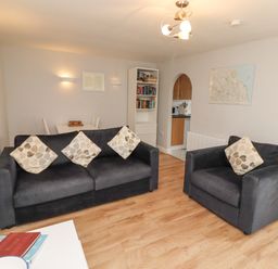 A living room with two sofas with patterned cushions a bookshelf a dining table and a map on the wall at Bedwine Cottage in Beadnell