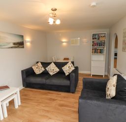 A living room with two black sofas with cushions a white bookshelf and a dining table at Bedwine Cottage in Beadnell