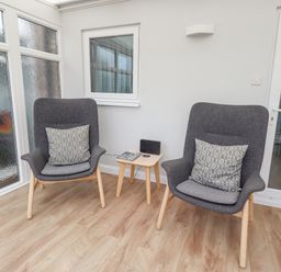 A seating area with two gray armchairs and a small wooden table between them at Bedwine Cottage in Beadnell