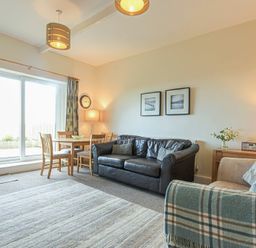 A living room with a black leather sofa a wooden dining table with chairs near sliding glass door and a beige armchair at Bellshill Cottage in Belford