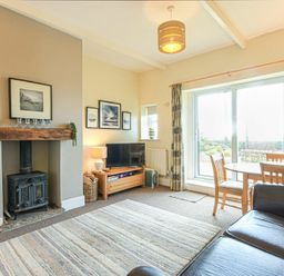 A living room with a wood stove and a dining table near sliding glass doors at Bellshill Cottage in Belford