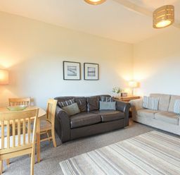 A living room with two sofas a wooden dining table with chairs and lamps at Bellshill Cottage in Belford