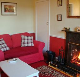 A living room with a red sofa a white coffee table and a fireplace at Briar Cottage in Town Yetholm and Kirk Yetholm