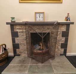 A fireplace with a metal fireguard and firewood a clock and sculptures on the mantel at Budle Bay Cottage in Bamburgh