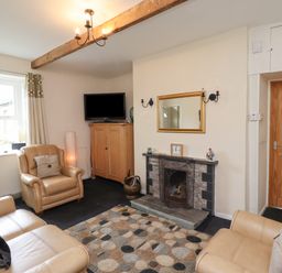 A living room with beige leather sofas a fireplace a wooden cabinet a television and a patterned rug at Budle Bay Cottage in Bamburgh