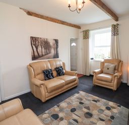 A living room with beige leather sofas a patterned rug and a window with curtains at Budle Bay Cottage in Bamburgh
