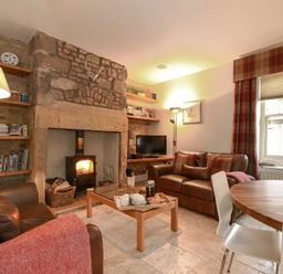 A living room with leather sofas a fireplace wooden shelves and a dining table at Coquet Cottage Warkworth