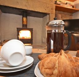 A tray with a French press, croissants, and cups in front of a wood stove fire in a living room at Coquet Cottage Warkworth