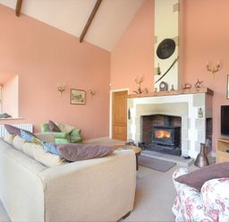 A living room with a fireplace a sofa an armchair a television and a window at Craster Tower Coach House in Craster
