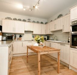 A kitchen with wooden cabinets a wooden table with flowers and kitchen appliances at Craster Tower Coach House in Craster