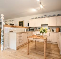 A kitchen with wooden cabinets a wooden table with flowers on it and various kitchen appliances at Craster Tower Coach House in Craster