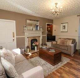A living room with two sofas a wooden coffee table a fireplace and a wooden door at Dray Cottage in Warkworth