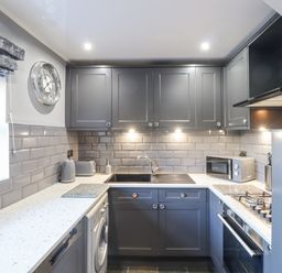 A kitchen with grey cabinets a clock on the wall and appliances at Dray Cottage in Warkworth