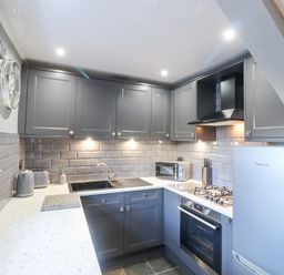 A kitchen with gray cabinets a sink a microwave stove and refrigerator at Dray Cottage in Warkworth
