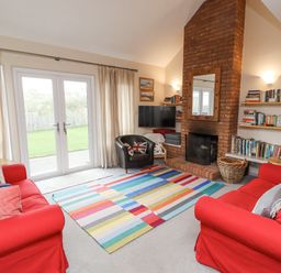 A living room with red sofas a colorful striped rug a brick fireplace and bookshelves at Dunes Cottage in Beadnell