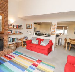A living room with a brick fireplace red sofas a multicolored striped rug bookshelf and a dining area with a wooden table and chairs at Dunes Cottage in Beadnell