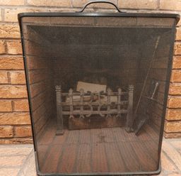 A fireplace with a black metal mesh screen and logs inside at Dunes Cottage in Beadnell