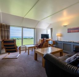 A living room with leather sofas wooden tables and chairs and a large window showing a green field and sea at Fidra in Embleton