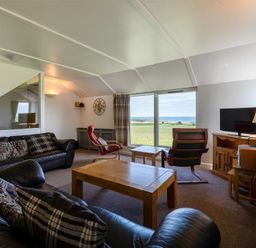 A living room with leather sofas and wooden tables facing a large window with a view at Fidra in Embleton